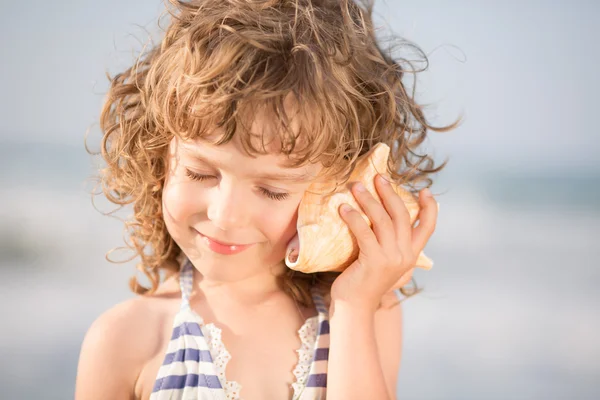 Bambino felice ascoltare conchiglia in spiaggia — Foto Stock