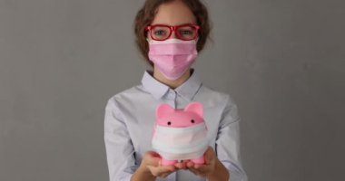 İş kadını elinde tıbbi maskeyle kumbarayı tutuyor. Coronavirus COVID-19 pandemik konsepti sırasında iş