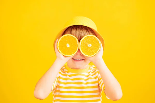 快乐的孩子拿着像太阳镜一样的橙子片 孩子穿着条纹黄色的T恤 背景是纸的 健康饮食和暑假概念 — 图库照片