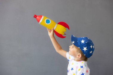 Mutlu çocuk beton duvar arkasında oyuncak roketle oynuyor. Çocuk astronot gibi davranıyor. Hayal gücü ve çocuklar rüya görür.