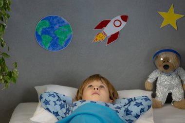Oyuncak roket ve oyuncak ayıyla uyuyan mutlu çocuk. Çocuk astronot gibi davranıyor. Hayal gücü ve çocuklar rüya görür.