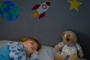 Oyuncak roket ve oyuncak ayıyla uyuyan mutlu çocuk. Çocuk astronot gibi davranıyor. Hayal gücü ve çocuklar rüya görür.