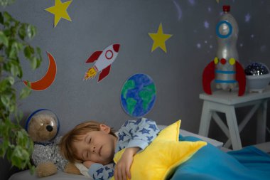 Oyuncak roket ve oyuncak ayıyla uyuyan mutlu çocuk. Çocuk astronot gibi davranıyor. Hayal gücü ve çocuklar rüya görür.