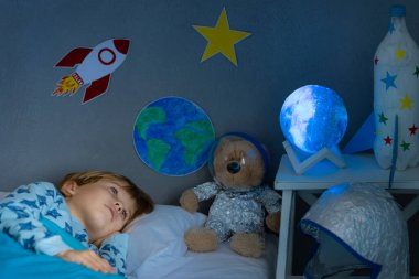 Oyuncak roket ve oyuncak ayıyla uyuyan mutlu çocuk. Çocuk astronot gibi davranıyor. Hayal gücü ve çocuklar rüya görür.