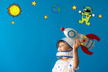 Mavi arka planda oyuncak roketle oynayan mutlu çocuk. Çocuk astronot gibi davranıyor. Hayal gücü ve çocuklar rüya görür.