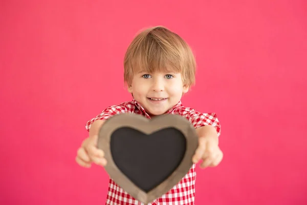 幸せな子供の心の形をした黒板を空白のまま ピンクの背景に笑顔の子供の肖像画 バレンタインデーの休暇のコンセプト — ストック写真