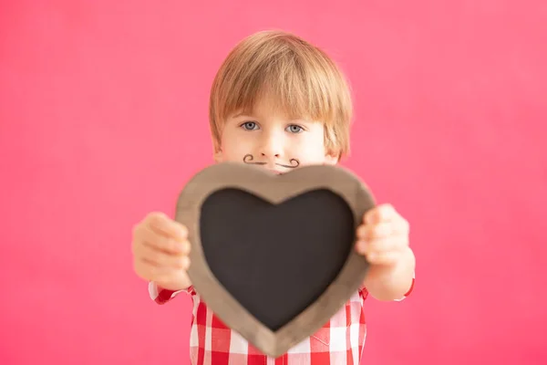 幸せな子供の心の形をした黒板を空白のまま ピンクの背景に笑顔の子供の肖像画 バレンタインデーの休暇のコンセプト — ストック写真