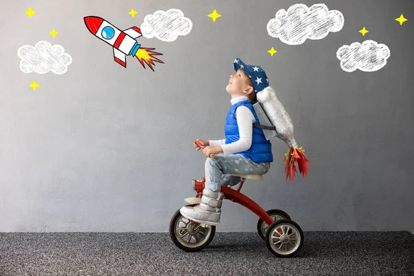 コンクリートの壁の背景におもちゃのロケットで遊ぶ幸せな子供 子供は宇宙飛行士のふりをする 子供用自転車 想像力と子供の夢のコンセプト — ストック写真
