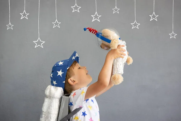おもちゃのロケットで遊ぶ幸せな子供 コンクリートの壁の背景にテディベアを持っている子供 男の子は宇宙飛行士のふりをする 想像力と子供の夢のコンセプト — ストック写真