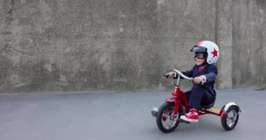 Mutlu çocuk iş adamı gibi davranıyor. Komik çocuk dışarıda trike kullanıyor. İşine dön, işe başla ve iş fikri kavramına dön. Yavaş çekim 4K