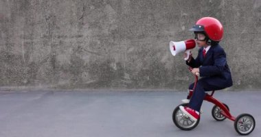 Mutlu çocuk iş adamı gibi davranıyor. Komik çocuk dışarıda trike kullanıyor. Hoparlörden bağıran çocuk. İşine dön, işe başla ve iş fikri kavramına dön. Yavaş çekim 4K