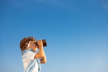 Çocuk mavi gökyüzüne dürbünle bakıyor. Yazın çocuk dışarıda eğleniyor. Macera ve seyahat konsepti