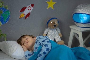 Oyuncak roket ve oyuncak ayıyla uyuyan mutlu çocuk. Çocuk astronot gibi davranıyor. Hayal gücü ve çocuklar rüya görür.