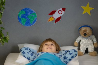 Oyuncak roket ve oyuncak ayıyla uyuyan mutlu çocuk. Çocuk astronot gibi davranıyor. Hayal gücü ve çocuklar rüya görür.