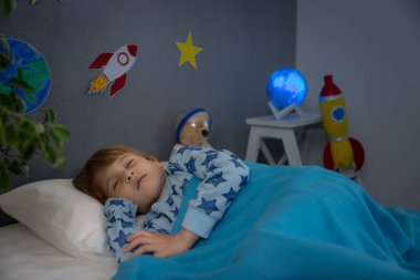 Oyuncak roket ve oyuncak ayıyla uyuyan mutlu çocuk. Çocuk astronot gibi davranıyor. Hayal gücü ve çocuklar rüya görür.