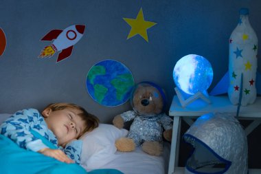 Oyuncak roket ve oyuncak ayıyla uyuyan mutlu çocuk. Çocuk astronot gibi davranıyor. Hayal gücü ve çocuklar rüya görür.
