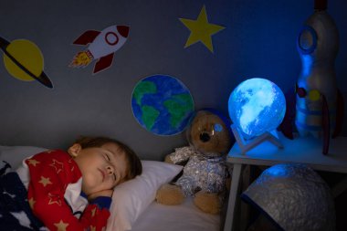 Oyuncak roket ve oyuncak ayıyla uyuyan mutlu çocuk. Çocuk astronot gibi davranıyor. Hayal gücü ve çocuklar rüya görür.