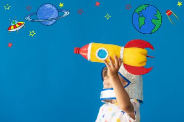 Mavi arka planda oyuncak roketle oynayan mutlu çocuk. Çocuk astronot gibi davranıyor. Hayal gücü ve çocuklar rüya görür.
