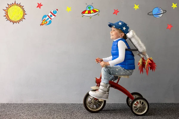 콘크리트 배경에 장난감 로켓을 가지고 한아이 비행사인 척하는 자전거타는 상상력 — 스톡 사진
