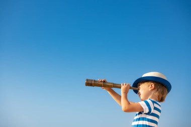 Mavi gökyüzüne karşı dürbünden bakan bir çocuk. Yazın çocuk dışarıda eğleniyor. Macera ve seyahat konsepti