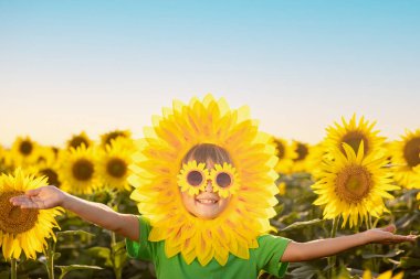 Mutlu çocuk bahar ayçiçeği tarlasında eğleniyor. Mavi arka planda komik bir çocuğun açık hava portresi