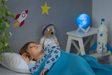 Oyuncak roket ve oyuncak ayıyla uyuyan mutlu çocuk. Çocuk astronot gibi davranıyor. Hayal gücü ve çocuklar rüya görür.