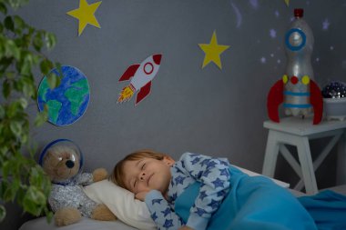 Oyuncak roket ve oyuncak ayıyla uyuyan mutlu çocuk. Çocuk astronot gibi davranıyor. Hayal gücü ve çocuklar rüya görür.