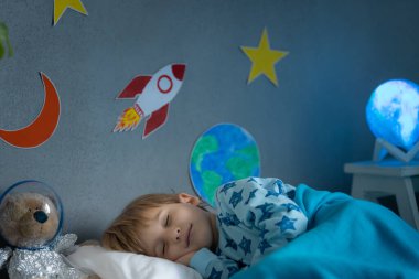 Oyuncak roket ve oyuncak ayıyla uyuyan mutlu çocuk. Çocuk astronot gibi davranıyor. Hayal gücü ve çocuklar rüya görür.