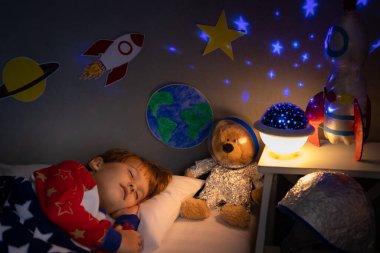 Oyuncak roket ve oyuncak ayıyla uyuyan mutlu çocuk. Çocuk astronot gibi davranıyor. Hayal gücü ve çocuklar rüya görür.