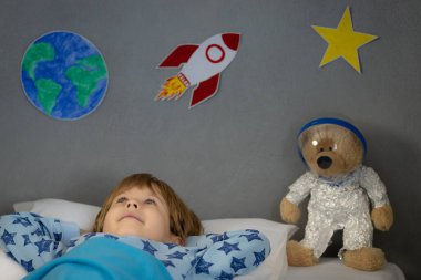 Oyuncak roket ve oyuncak ayıyla uyuyan mutlu çocuk. Çocuk astronot gibi davranıyor. Hayal gücü ve çocuklar rüya görür.