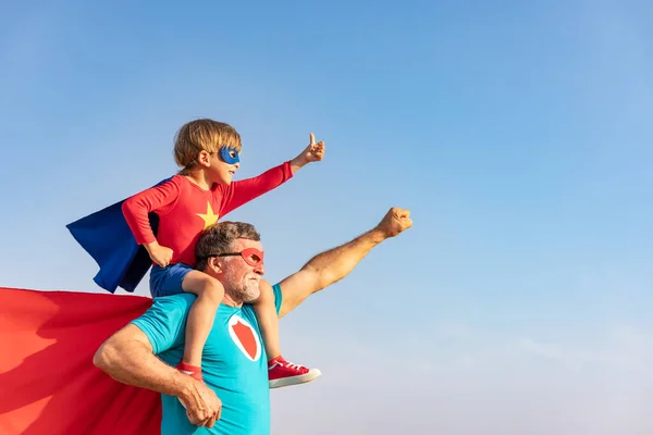 スーパーヒーローの先輩と子供が屋外で遊んでいます 青い空を背景に一緒に楽しむスーパーヒーローの祖父と少年 家族の休日の概念 幸せな父の日 — ストック写真