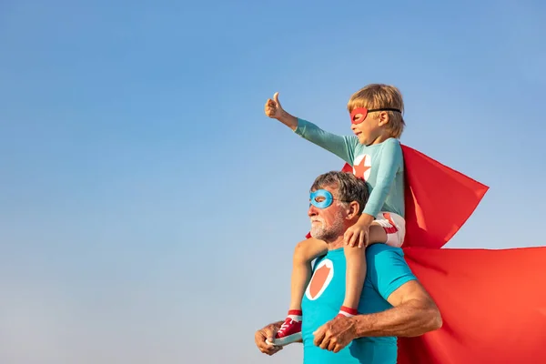 スーパーヒーローの先輩と子供が屋外で遊んでいます 青い夏の空を背景に一緒に楽しむスーパーヒーローの祖父と少年 家族の休日の概念 幸せな父の日 — ストック写真