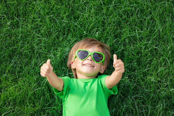 春の公園で屋外で遊んで幸せな子供 緑の草の上に寝そべって 地球の日と生態学の概念 親指を立てる少年 — ストック写真