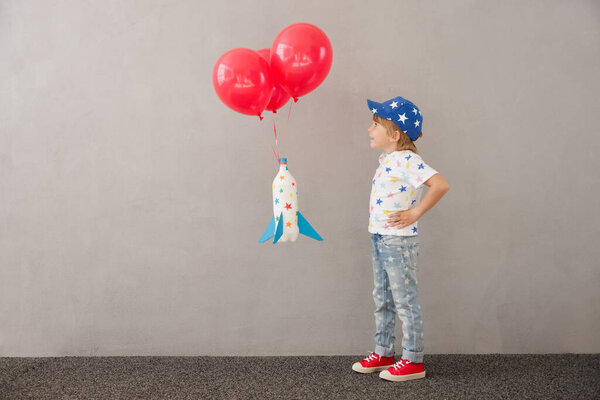 Happy child playing with toy rocket at home. Kid pretend to be astronaut. Imagination and children dream concept