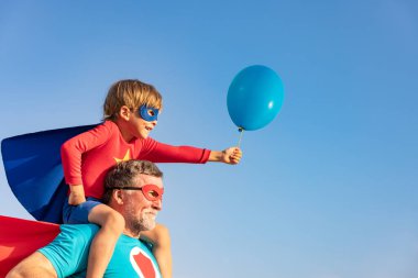 Süper kahraman kıdemli adam ve çocuk dışarıda oynuyorlar. Süper kahraman büyükbaba ve çocuk mavi gökyüzü geçmişine karşı birlikte eğleniyorlar. Aile tatili konsepti. Babalar günün kutlu olsun.