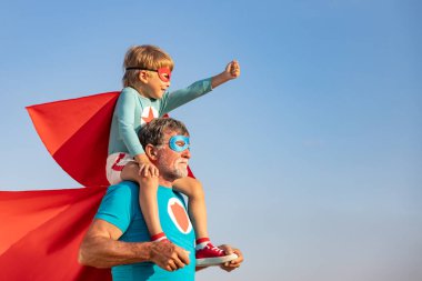 Süper kahraman kıdemli adam ve çocuk dışarıda oynuyorlar. Süper kahraman büyükbaba ve çocuk mavi gökyüzü geçmişine karşı birlikte eğleniyorlar. Aile tatili konsepti. Babalar günün kutlu olsun.