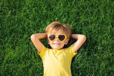 Mutlu çocuk bahar parkında dışarıda oynuyor. Çocuk yeşil çimlerin üzerinde yatıyor. Dünya günü ve ekoloji konsepti. Dışarıdaki oğlanın en iyi portresi.