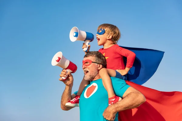 超级英雄老年人和孩子在户外玩耍 超级英雄爷爷和男孩在蓝色的夏日天空背景下 通过扩音器大喊 家庭假期的概念 父亲节快乐 — 图库照片