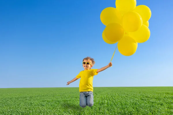 緑の春のフィールドにジャンプする幸せな子供 青い空を背景に黄色い風船の子供 自由と自由の屋外 — ストック写真