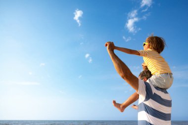 Mutlu aile sahilde eğleniyor. Baba ve oğul mavi deniz ve gökyüzü arka planına karşı. Yaz tatili ve babalar günü konsepti. Dikiz görünümü portresi