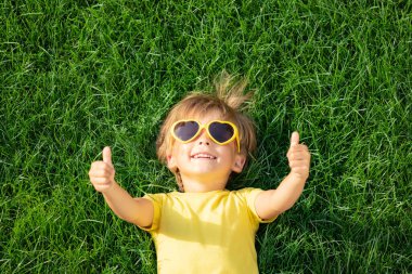 Mutlu çocuk bahar parkında dışarıda oynuyor. Çocuk yeşil çimlerin üzerinde yatıyor. Dünya günü ve ekoloji konsepti. Başparmak gösteren çocuk