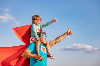 Süper kahraman kıdemli adam ve çocuk dışarıda oynuyorlar. Süper kahraman büyükbaba ve çocuk mavi gökyüzü geçmişine karşı birlikte eğleniyorlar. Aile tatili konsepti. Babalar günün kutlu olsun.
