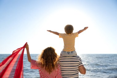 Mutlu aile sahilde eğleniyor. Anne, baba ve çocuk mavi deniz ve gökyüzü arka planına karşı. Yaz tatili kavramı. Dikiz görünümü portresi