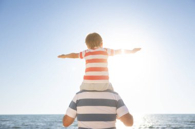 Mutlu aile sahilde eğleniyor. Baba ve oğul mavi deniz ve gökyüzü arka planına karşı. Yaz tatili ve babalar günü konsepti. Dikiz görünümü portresi
