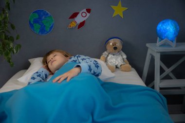 Oyuncak roket ve oyuncak ayıyla uyuyan mutlu çocuk. Çocuk astronot gibi davranıyor. Hayal gücü ve çocuklar rüya görür.