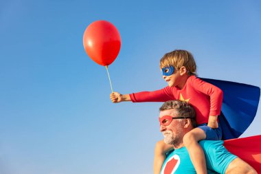 Süper kahraman kıdemli adam ve çocuk dışarıda oynuyorlar. Süper kahraman büyükbaba ve çocuk mavi gökyüzü geçmişine karşı birlikte eğleniyorlar. Aile tatili konsepti. Babalar günün kutlu olsun.