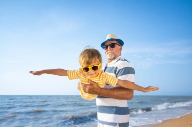 Mutlu aile sahilde eğleniyor. Büyükbaba ve çocuk mavi denize ve gökyüzüne karşı. Yaz tatili ve Babalar Günü konsepti