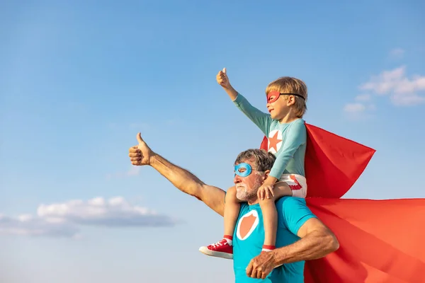 超级英雄老年人和孩子在户外玩耍 超级英雄爷爷和男孩一起在蓝色的夏日天空背景下玩乐 家庭假期的概念 父亲节快乐 — 图库照片