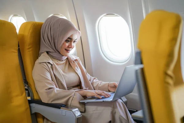 Beautiful asian muslim business woman working on digital laptop computer during the flight for her business trip. Business and transportation concept.