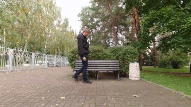 Um homem senta-se num banco no parque — Vídeo de Stock